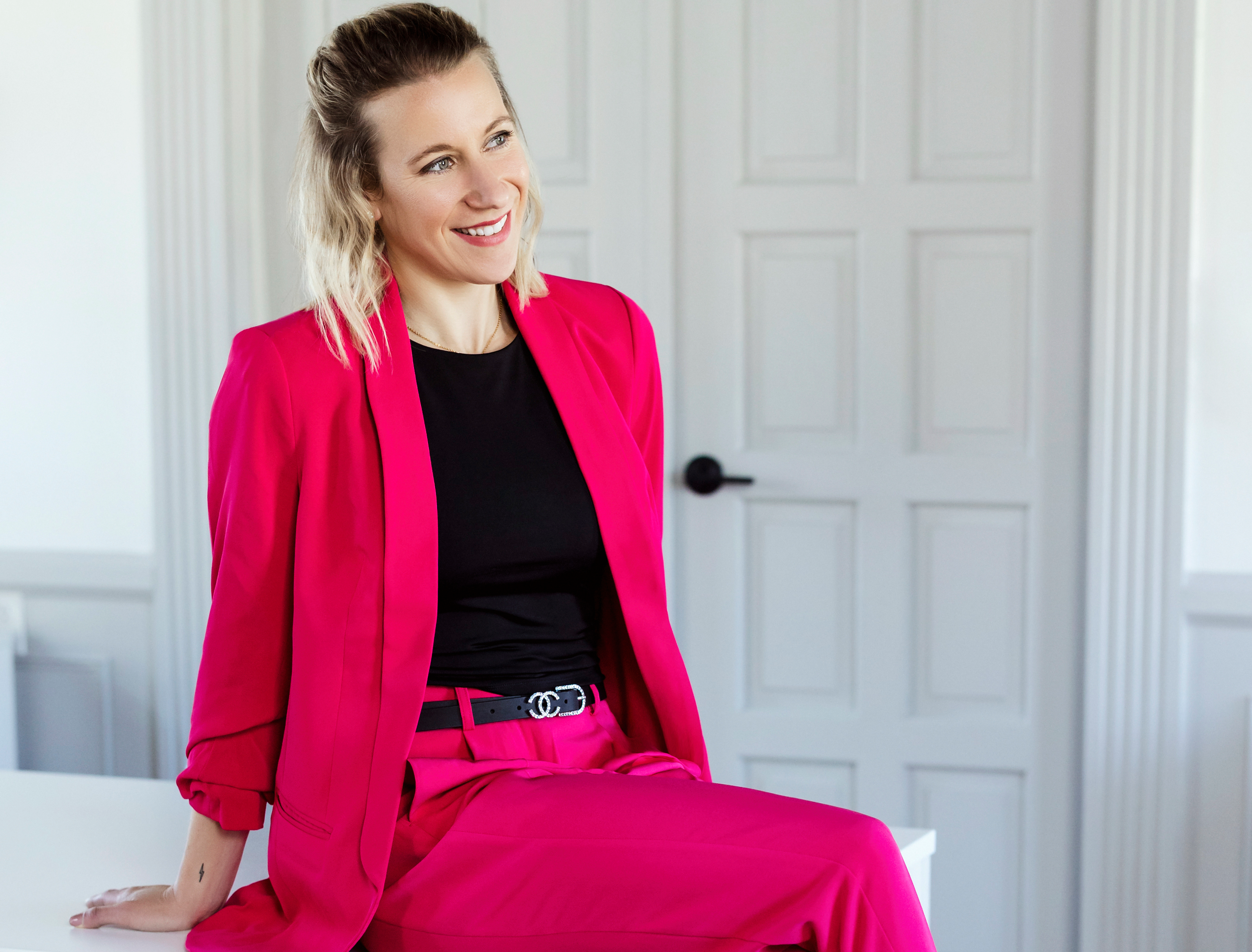 Nicholle sitting on her desk in a magenta suit