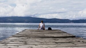 A woman sitting on the edge of a wooden plank infront of the ocean looking over the other island.