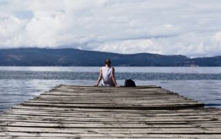 A woman sitting on the edge of a wooden plank infront of the ocean looking over the other island.