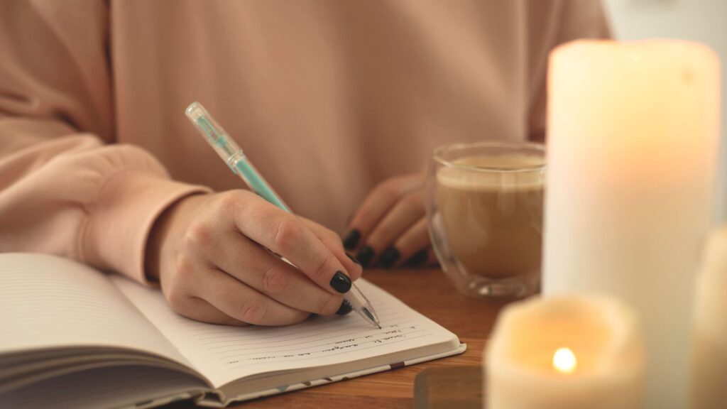 A confident, stylish woman writing in a journal at a cozy table with coffee, sunlight pouring in, reflecting on her money mindset. The setting is soft, warm, empowering, and feminine