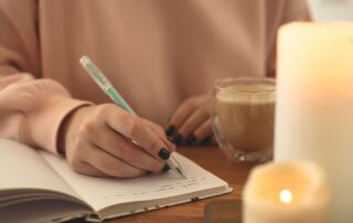 A confident, stylish woman writing in a journal at a cozy table with coffee, sunlight pouring in, reflecting on her money mindset. The setting is soft, warm, empowering, and feminine